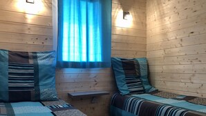 A cozy cabin room with two beds, a window with curtains, and a wooden wall.