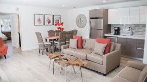 En moderne stue med en beige sofa, et spisebord med fletstole og et køkkenområde med rustfrie stålgadgetter.