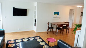 Una sala de estar con un televisor de pantalla plana, una mesa de comedor con sillas, una alfombra colorida y un sofá de cuero negro.