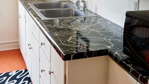 Una cocina con armarios blancos, encimera de mármol negro, pileta doble y microondas.