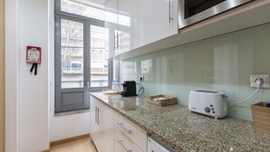 A kitchen with white cabinets, a granite countertop, a toaster, and a window with a view of buildings outside. - Feel Corporate Housing Marquês I (Oporto)