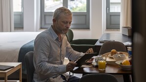 A man sitting at a table with a tablet, a glass of orange juice, and a bowl of fruit. - Feel Corporate Housing Marquês I (Oporto)