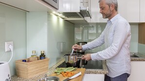 A modern kitchen with a person cooking, a wooden spice rack, and a cutting board with vegetables. - Feel Corporate Housing Marquês I (Oporto)