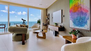 Una sala de estar moderna con un amplio ventanal con vistas al mar, un ventilador de techo y un cuadro abstracto y colorido.