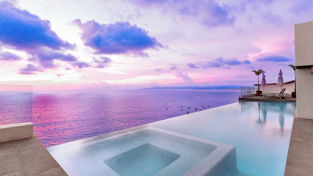 Una piscina infinita con vistas despejadas al mar y un cielo al atardecer.