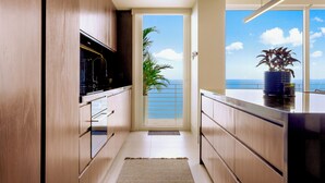 A modern kitchen with wooden cabinets, a black countertop, and a view of the ocean through a glass door. - Romantic Zone Luxury Ocean-View Condo w/Rooftop Infinity Pool. Walk to Beach! (Puerto Vallarta)