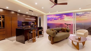 Una sala de estar moderna con cocina, un ventanal con vistas al atardecer, un ventilador de techo y una mesa de centro redonda.