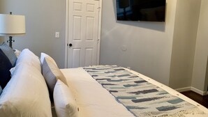 A bedroom with a bed, a TV mounted on the wall, and a door. - Cozy Apartment in the Heart of MainStrasse (Covington)