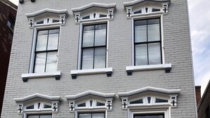 A gray building with six windows, a red door, and a brick facade. - Cozy Apartment in the Heart of MainStrasse (Covington)