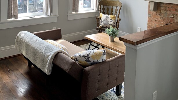 A living room with a fireplace, a ceiling fan, and a large window. - Cozy Apartment in the Heart of MainStrasse (Covington)
