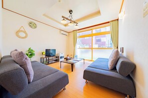 A modern living room with two grey sofas, a wooden coffee table, a flat-screen TV, and a large window with curtains.