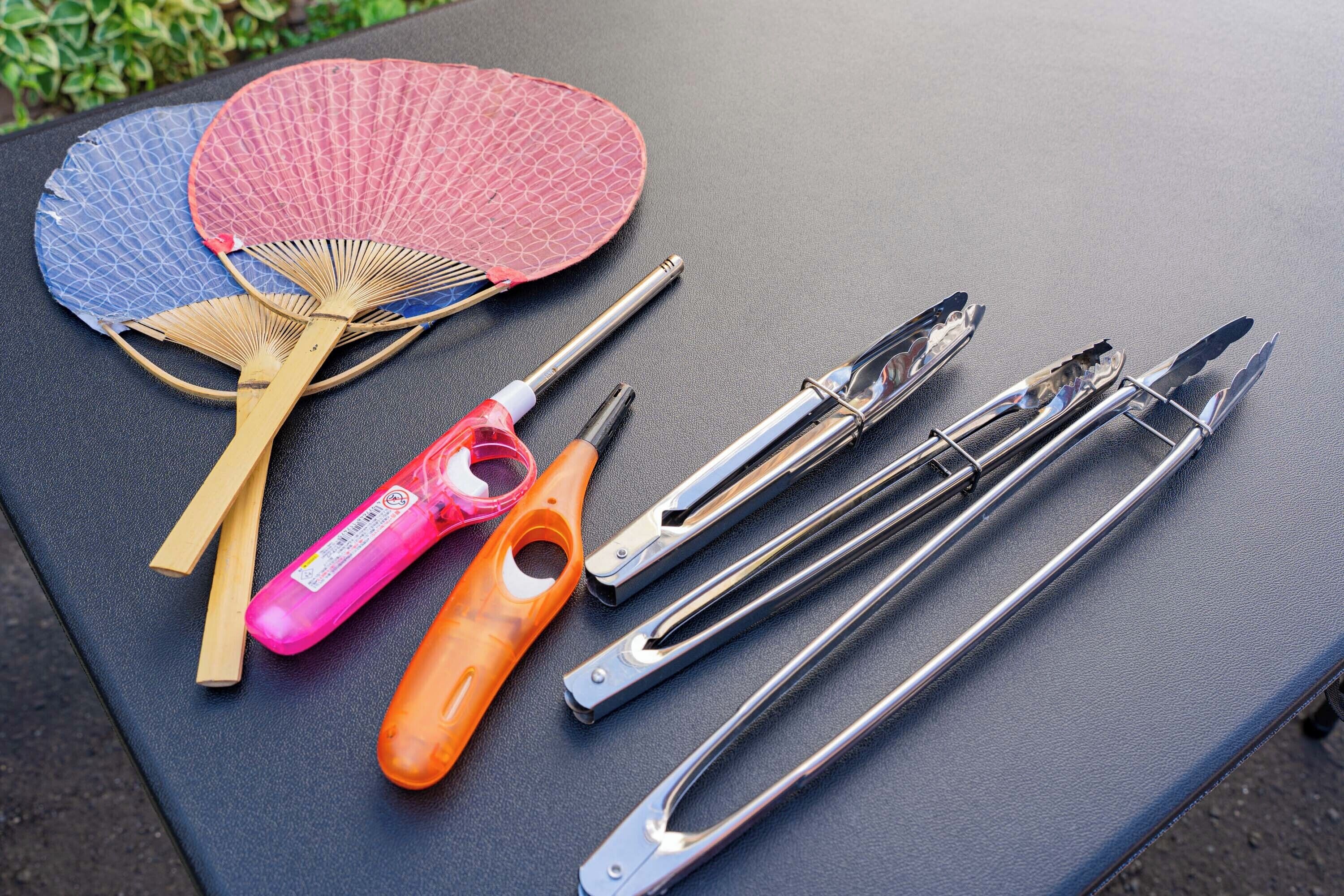 A table with a blue and pink fan, a wooden fan, a pink and orange bottle opener, and a set of metal tools.