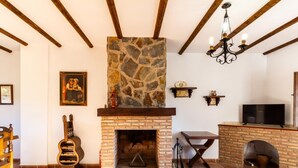 A cozy living room with a stone fireplace, wooden beams, a television, and a guitar. - Complex of 3 apartments with swimming pool (Melegís)