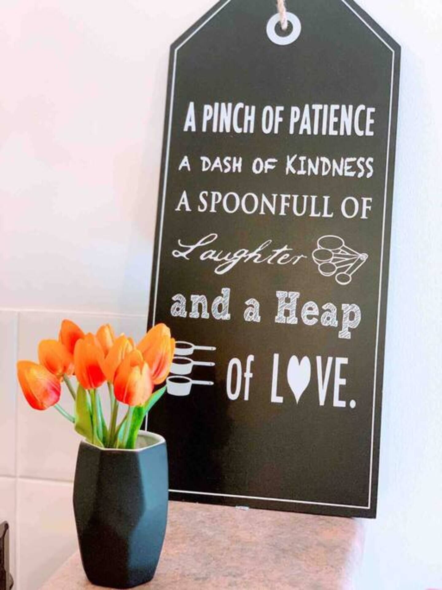 A decorative sign with a message about love and patience, placed above a vase of orange tulips.