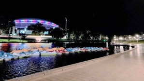 Een waterkant met een groot verlicht stadion en een rij kleine bootjes.