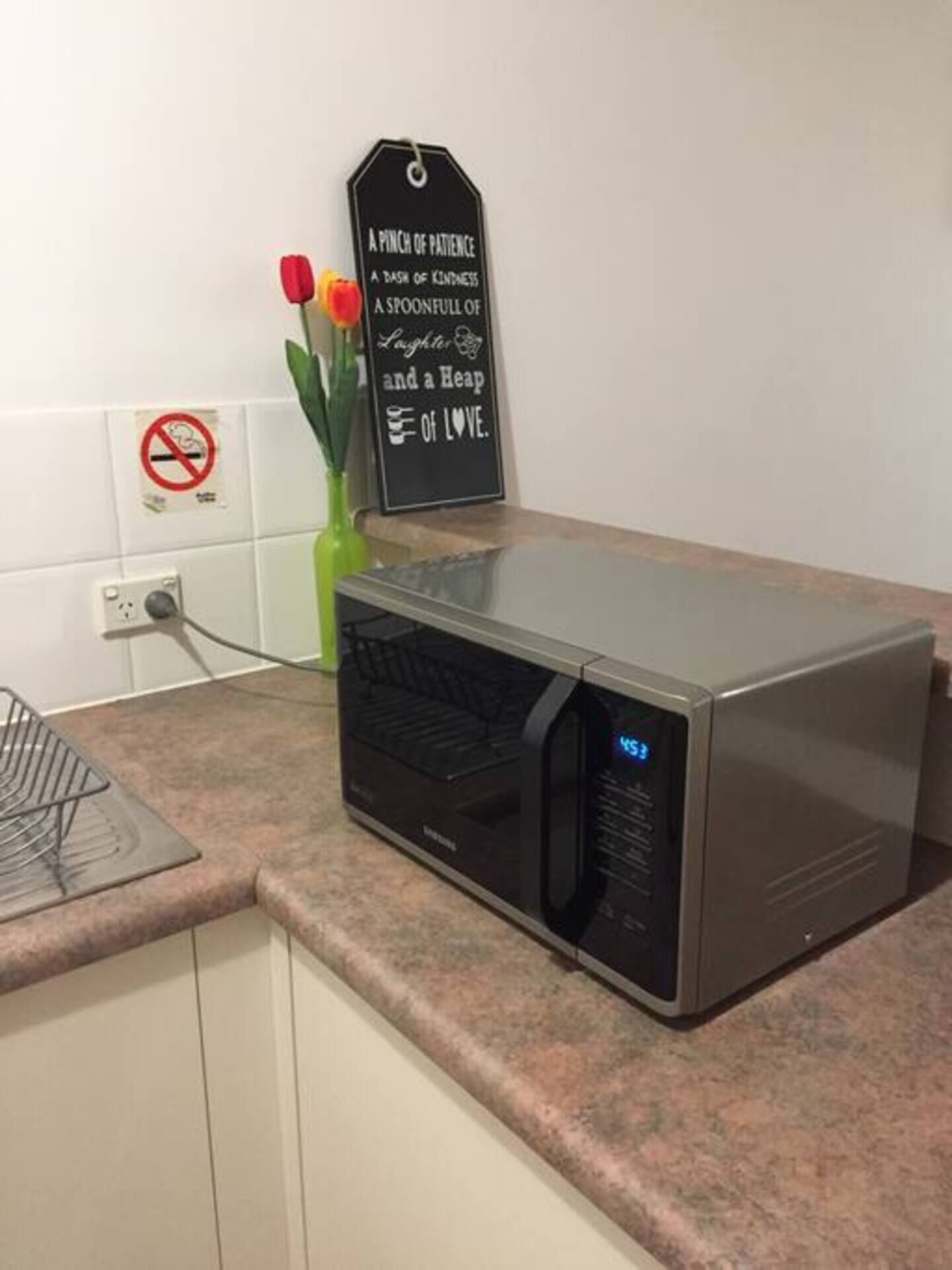 Une cuisine avec un four à micro-ondes sur le comptoir, un panneau affichant un message et un panneau « interdiction de fumer » sur le mur.