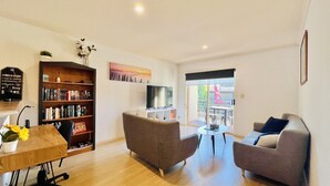 Een moderne woonkamer met een houten salontafel, twee grijze banken, een boekenkast, een flatscreen televisie en een groot raam met uitzicht.