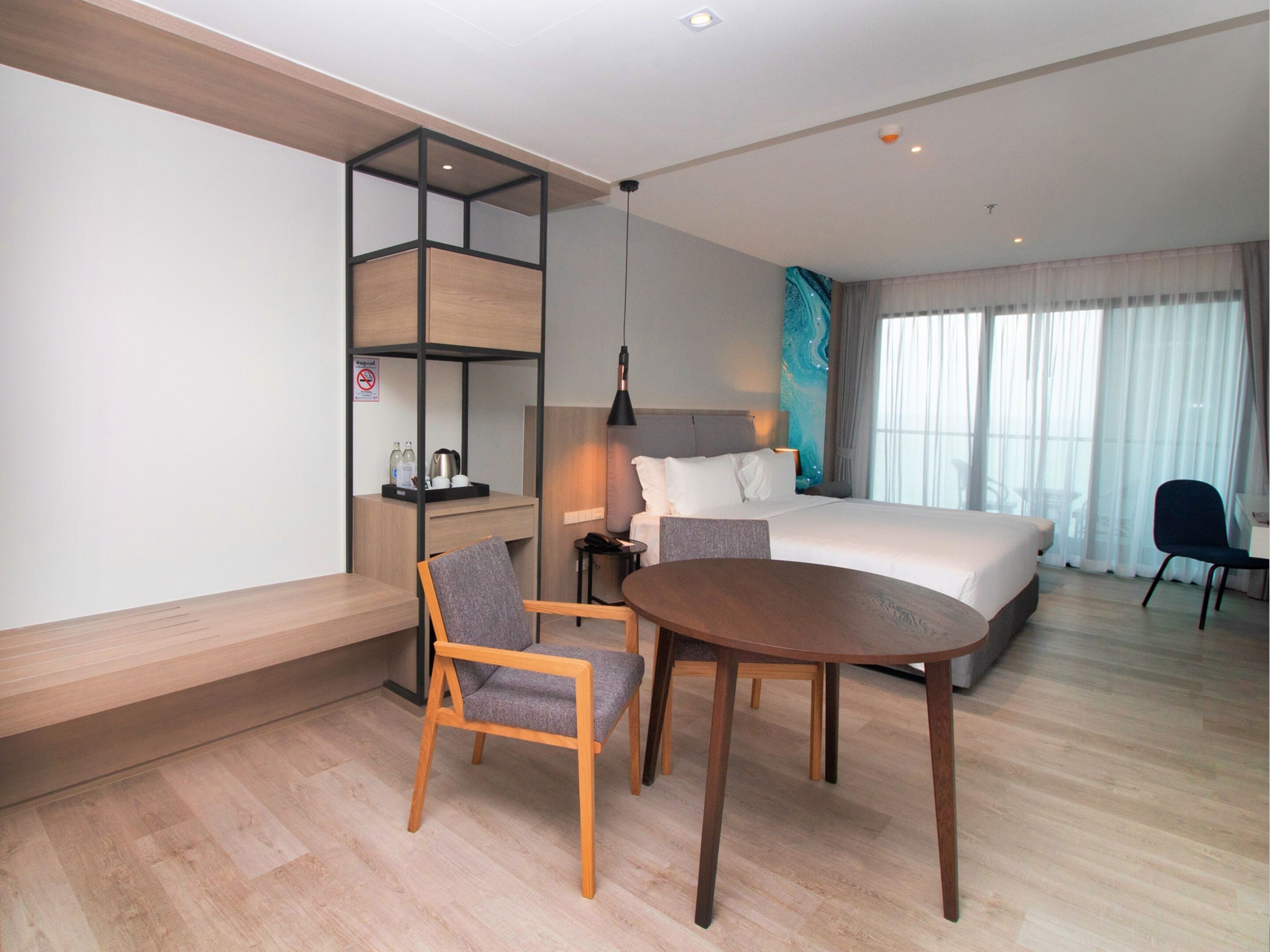 A modern hotel room with a bed, a desk, a chair, a small table, and a bookshelf.