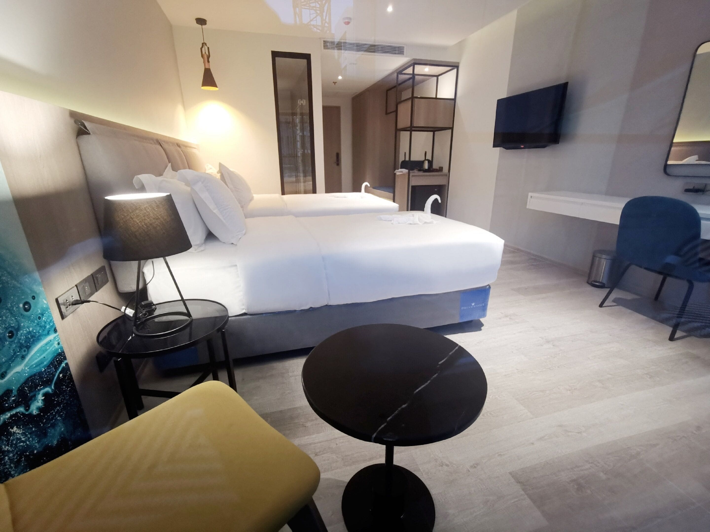 A modern hotel room with a bed, bedside table, lamp, chair, and a TV mounted on the wall.