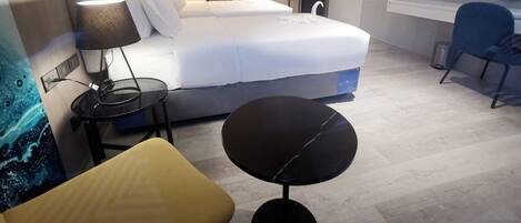A modern hotel room with a bed, bedside table, lamp, chair, and a TV mounted on the wall.