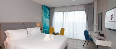 Una habitación de hotel moderna con una cama grande, un escritorio, una silla y un televisor que muestra el logotipo de Fortune Hotel Group.