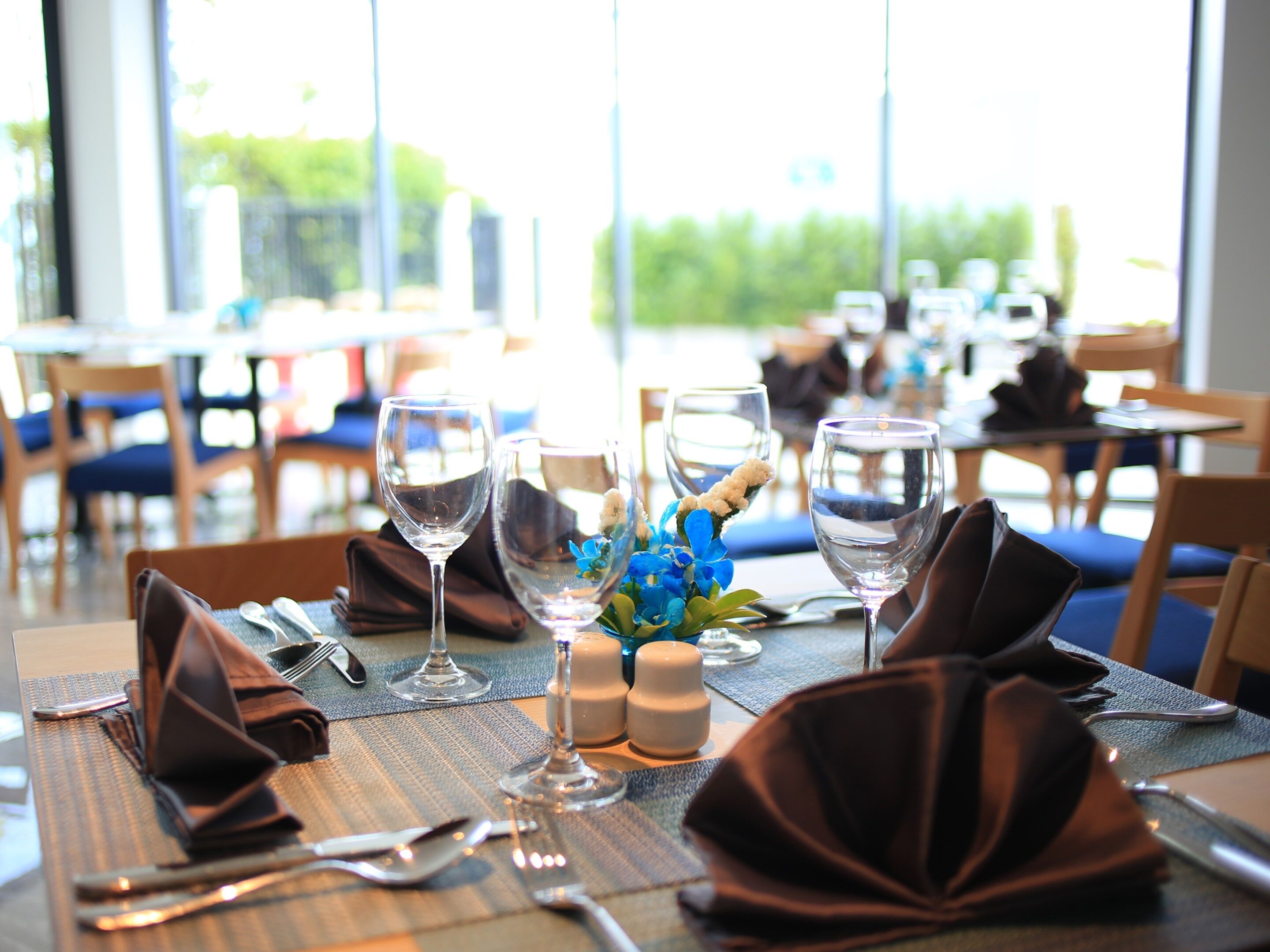 Un ambiente de restaurante con mesas dispuestas para comer, destacando copas de cristal transparente y centros de mesa con flores azules.