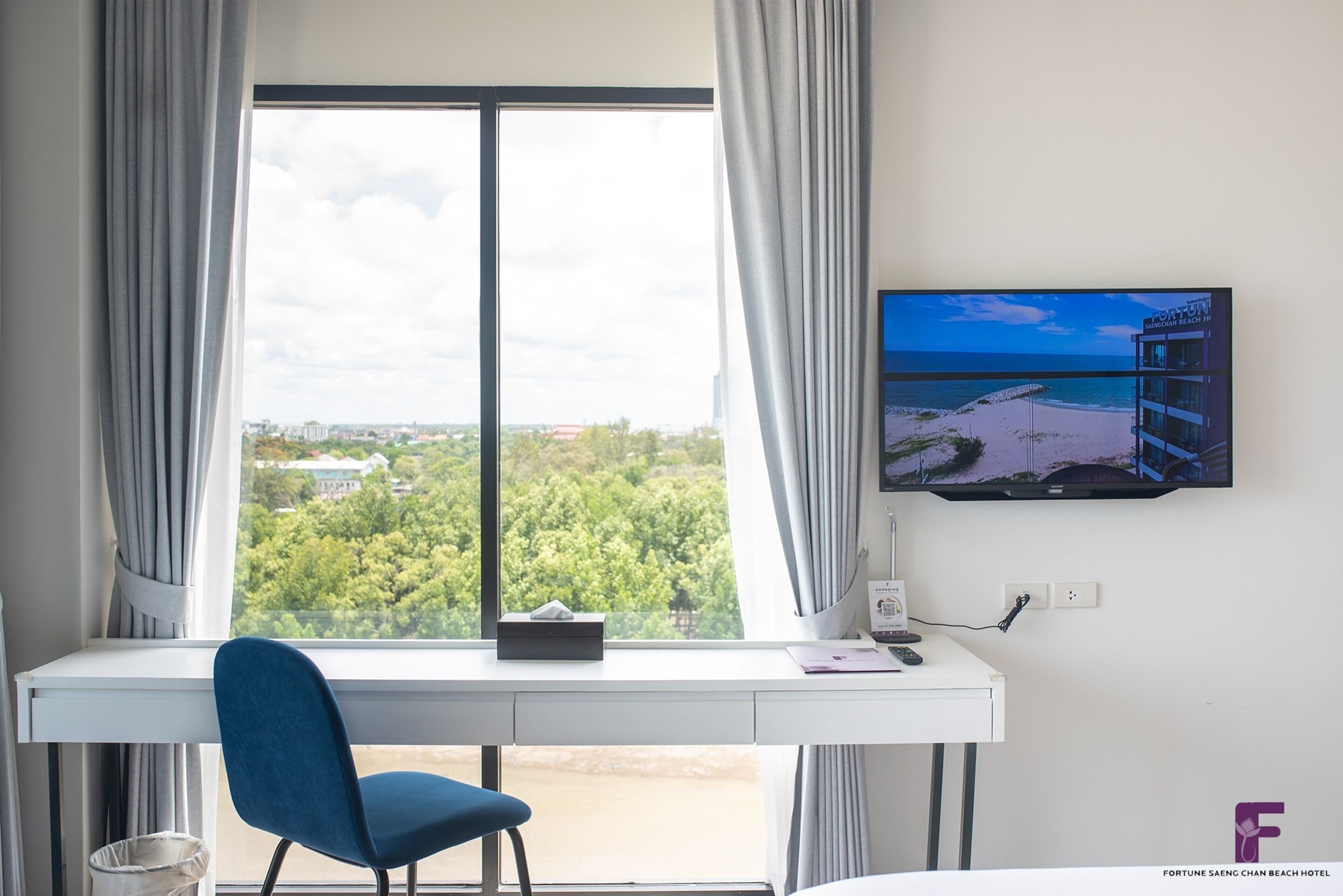 A hotel room with a desk, chair, and a TV displaying a beach view.