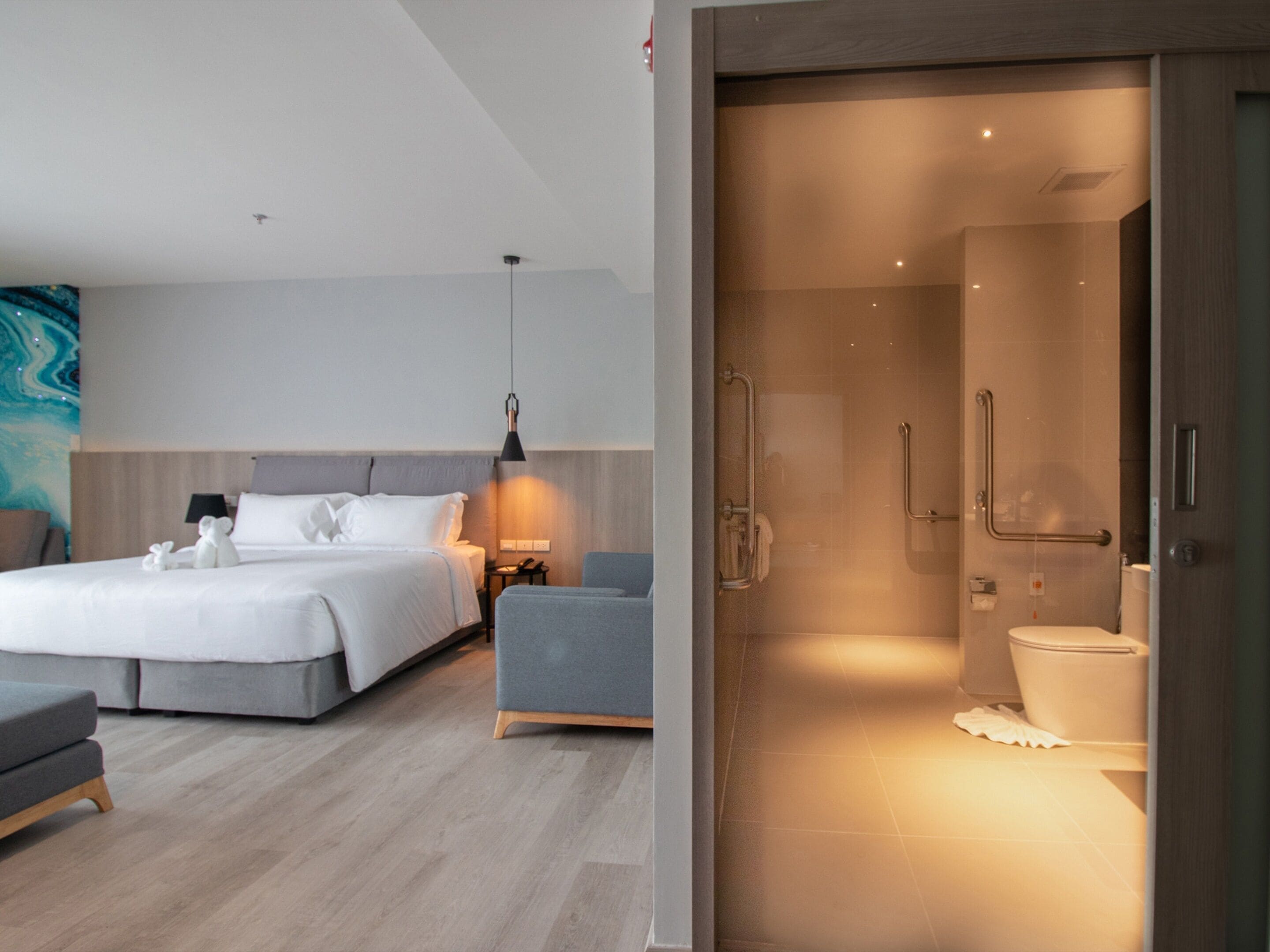 Een moderne hotelkamer met een groot bed, nachtkastje, stoel en een aparte badkamer met douche en toilet.