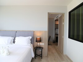 Camera d'albergo con un letto, una lampada da comodino, un tavolino e vista su un corridoio che porta a un armadio.