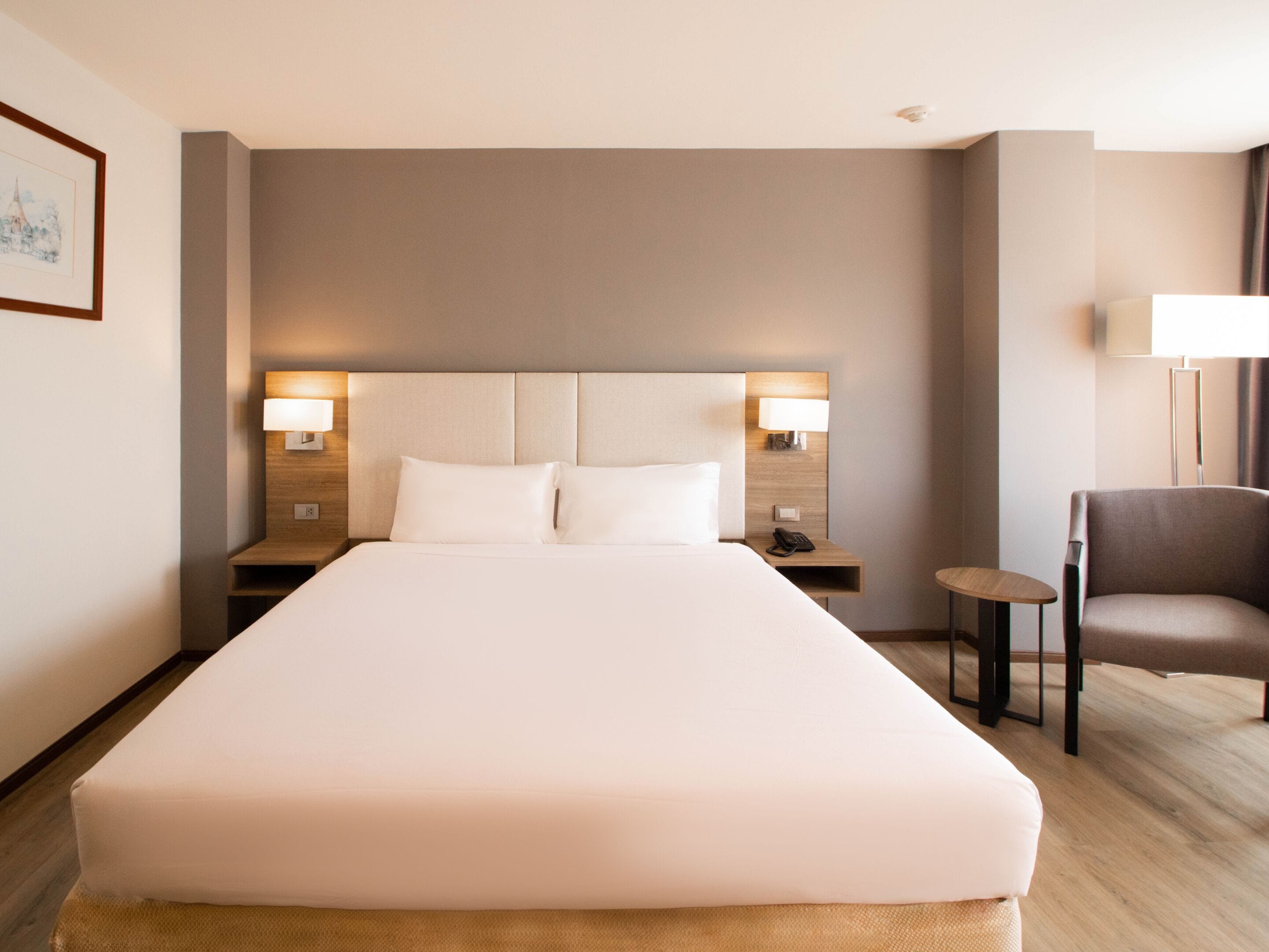 A hotel room with a large bed, two bedside lamps, a chair, and a small table.