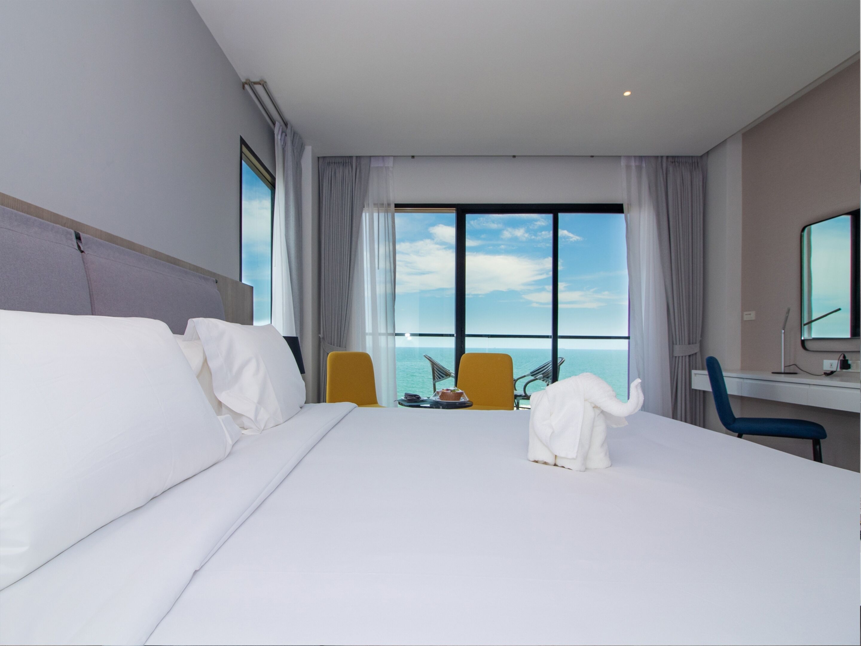 A hotel room with a large bed, a desk, a chair, and a view of the ocean.