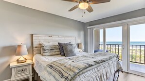 Ein Schlafzimmer mit einem Bett, einem Nachttisch, einem Deckenventilator und Meerblick durch große Fenster.