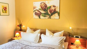 A hotel room with a bed, two bedside tables, a nightstand, a lamp, a painting of tulips, and a vase with flowers. - Am Hohen Bogen by Interhome (Arrach)