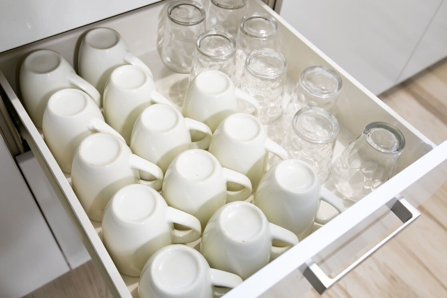 A drawer filled with white ceramic mugs and clear glass tumblers.