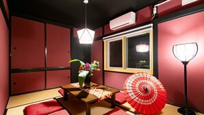 Een traditionele Japanse kamer met tatami vloeren, een lage tafel met een bloevas, een rode paraplu en een raam met uitzicht op groen.