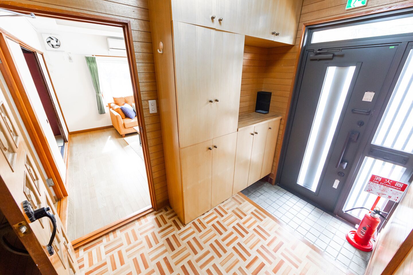 A hotel room with wooden flooring, a sofa, cabinets, and a fire extinguisher.