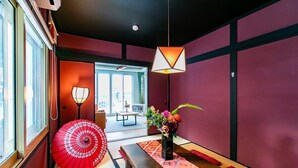 Een kamer met tatami vloerbedekking, een traditionele Japanse lamp, een rode paraplu en een vaas met bloemen.