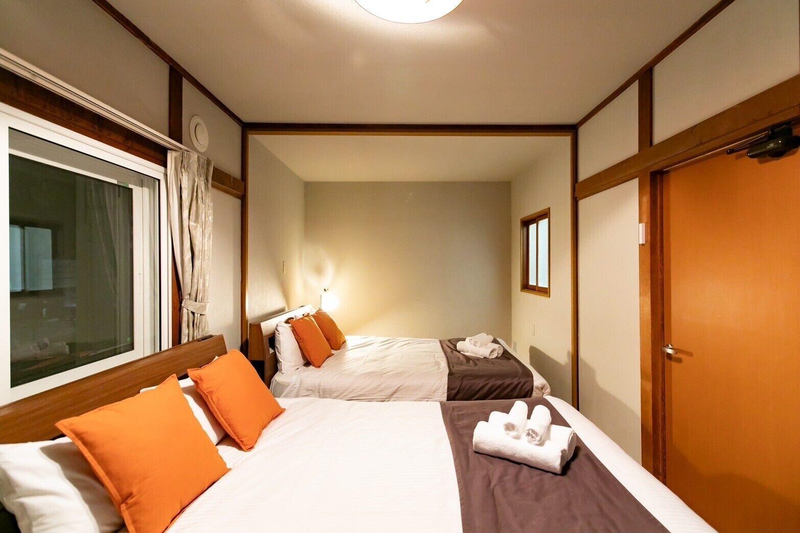 Une chambre d’hôtel avec deux lits, une fenêtre avec des rideaux, une porte et une petite fenêtre sur le mur.