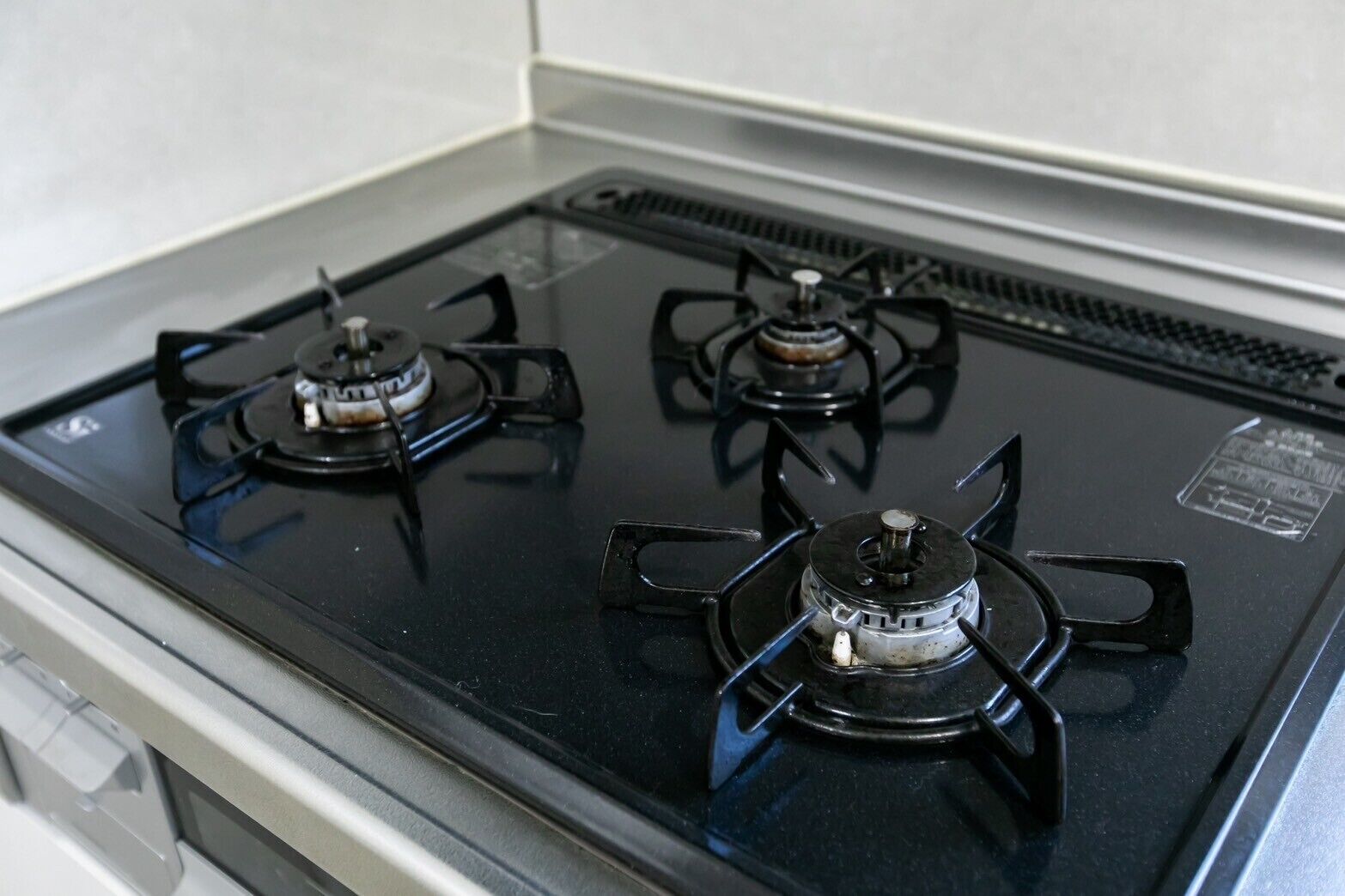 Una cocina con tres estufas de gas negras y una campana extractora de acero inoxidable.