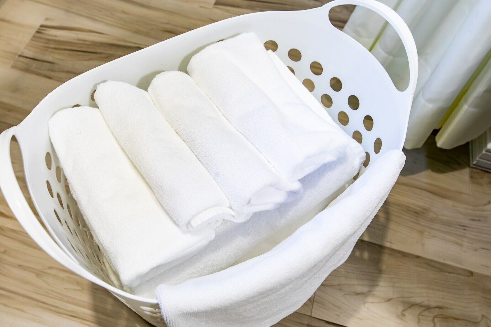 A white plastic basket containing folded white towels.