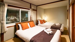 Een hotelkamer met twee bedden, een groot raam met gordijnen, een bedlampje en uitzicht op gebouwen.