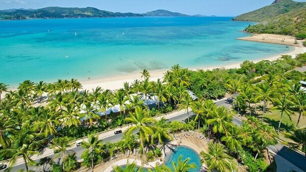 A resort with a beach, palm trees, and a swimming pool.