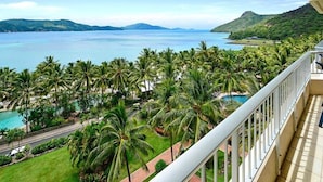 A balcony with a view of a tropical resort, including a swimming pool and palm trees.