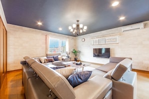 A modern living room with a sectional sofa, a flat-screen TV, and a chandelier. - The Worldwide House (Sapporo)
