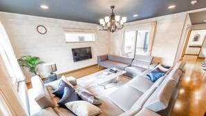 Un salon moderne avec un canapé d’angle, un téléviseur à écran plat et un lustre.