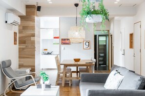 A modern living room with a grey sofa, a dining table with chairs, and a hanging plant. - The East Avenue (Sapporo)