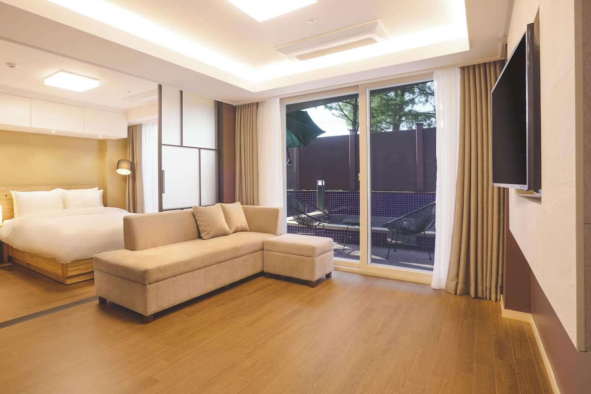Una habitación de hotel moderna con cama, sofá y un balcón con mobiliario exterior.