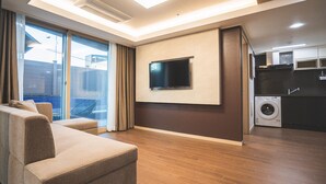 Een moderne woonkamer met een flatscreen televisie aan de muur, een bank en een schuifpui naar een balkon.