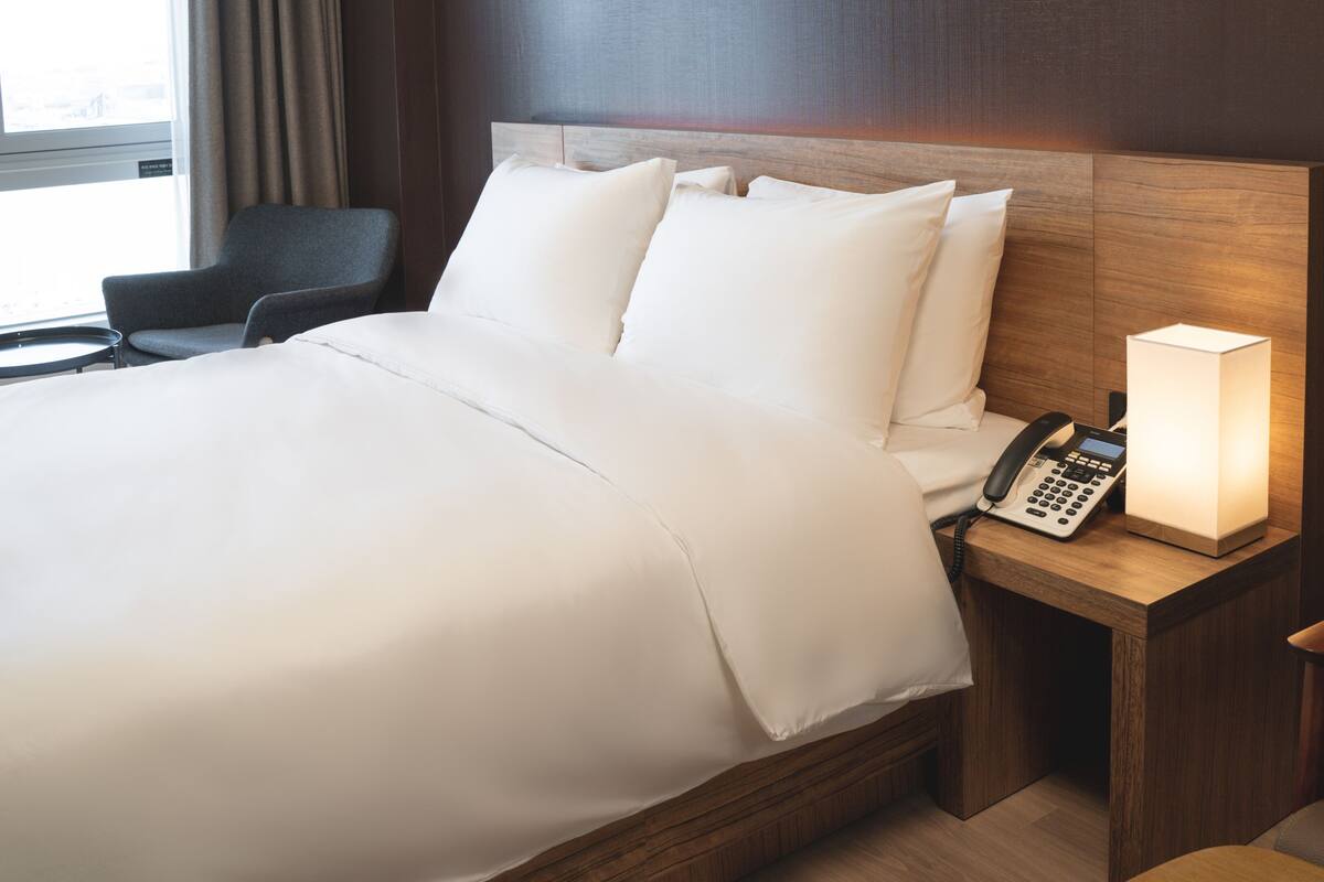 Una habitación de hotel con una cama grande, teléfono en la mesita de noche y una lámpara.
