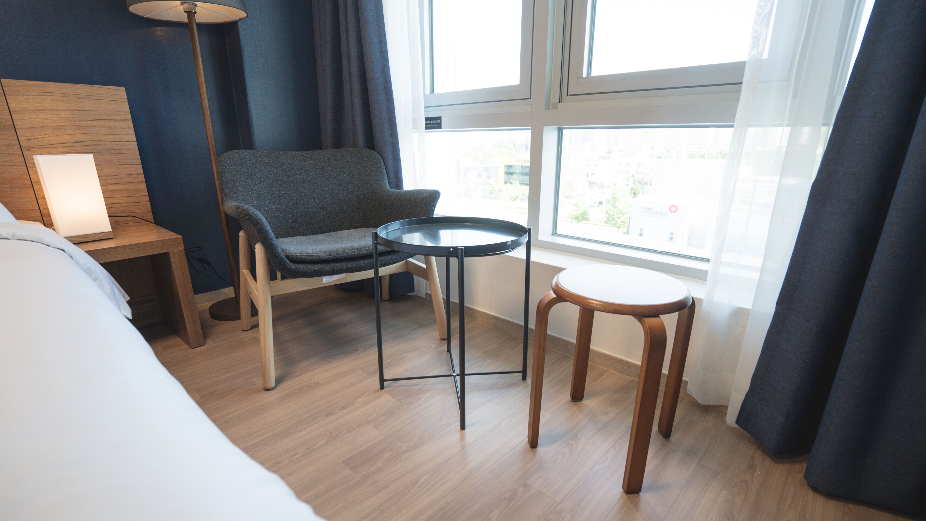 A hotel room with a bed, a desk, a chair, a small table, and a window with curtains.